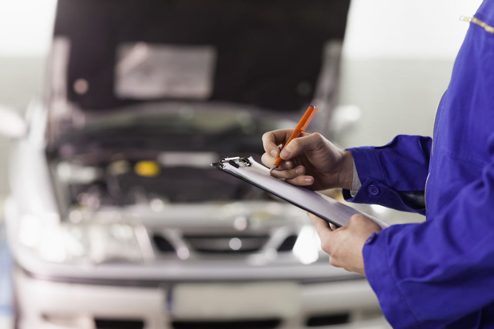 Close up of a man writing on a clipboard in a garage the best auto mechanic in San Diego
